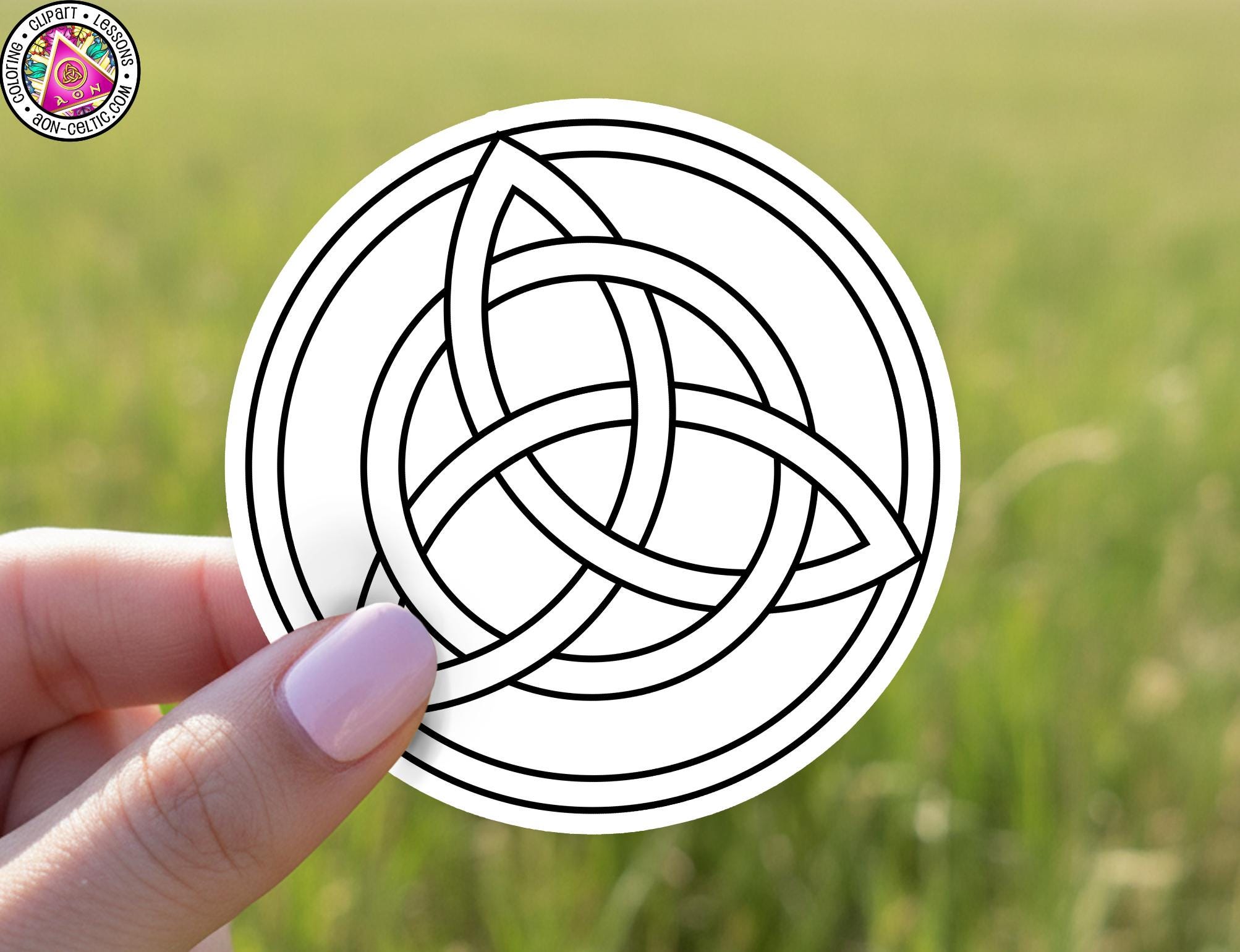 A hand holding a circular sticker with a black and white design of a knot or symbol.