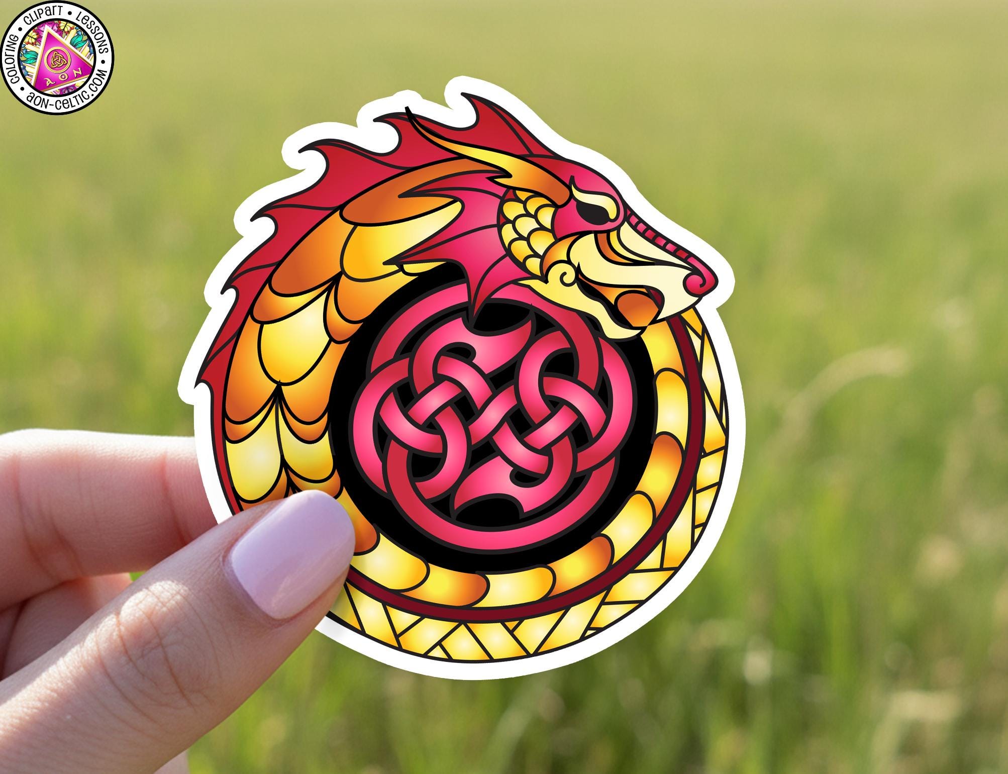 A hand holding a sticker featuring a colorful dragon design with a Celtic knot pattern.