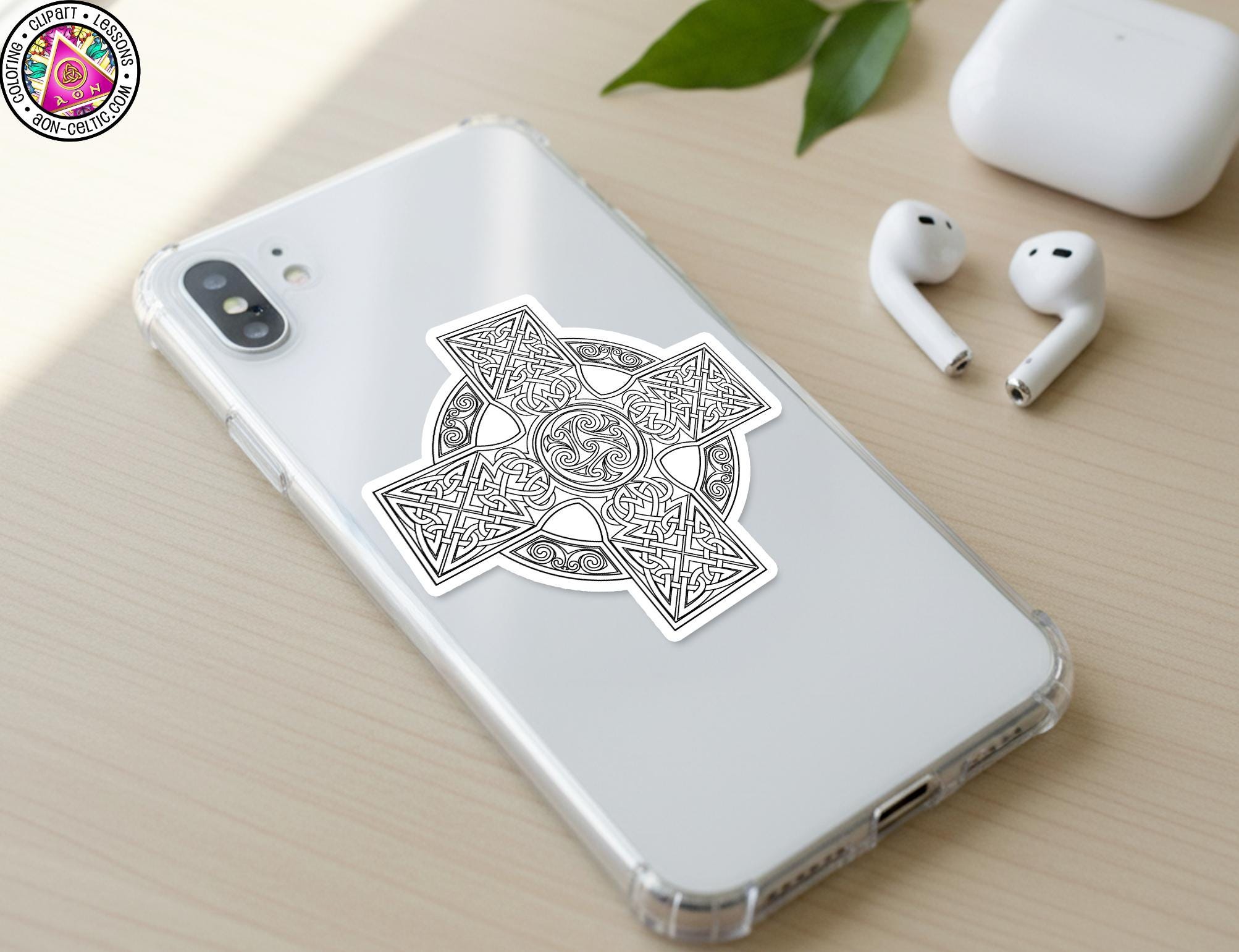 a smartphone with a sticker of a Celtic knot design on its back cover, along with a pair of white earbuds and a white charging cable on a wooden surface.