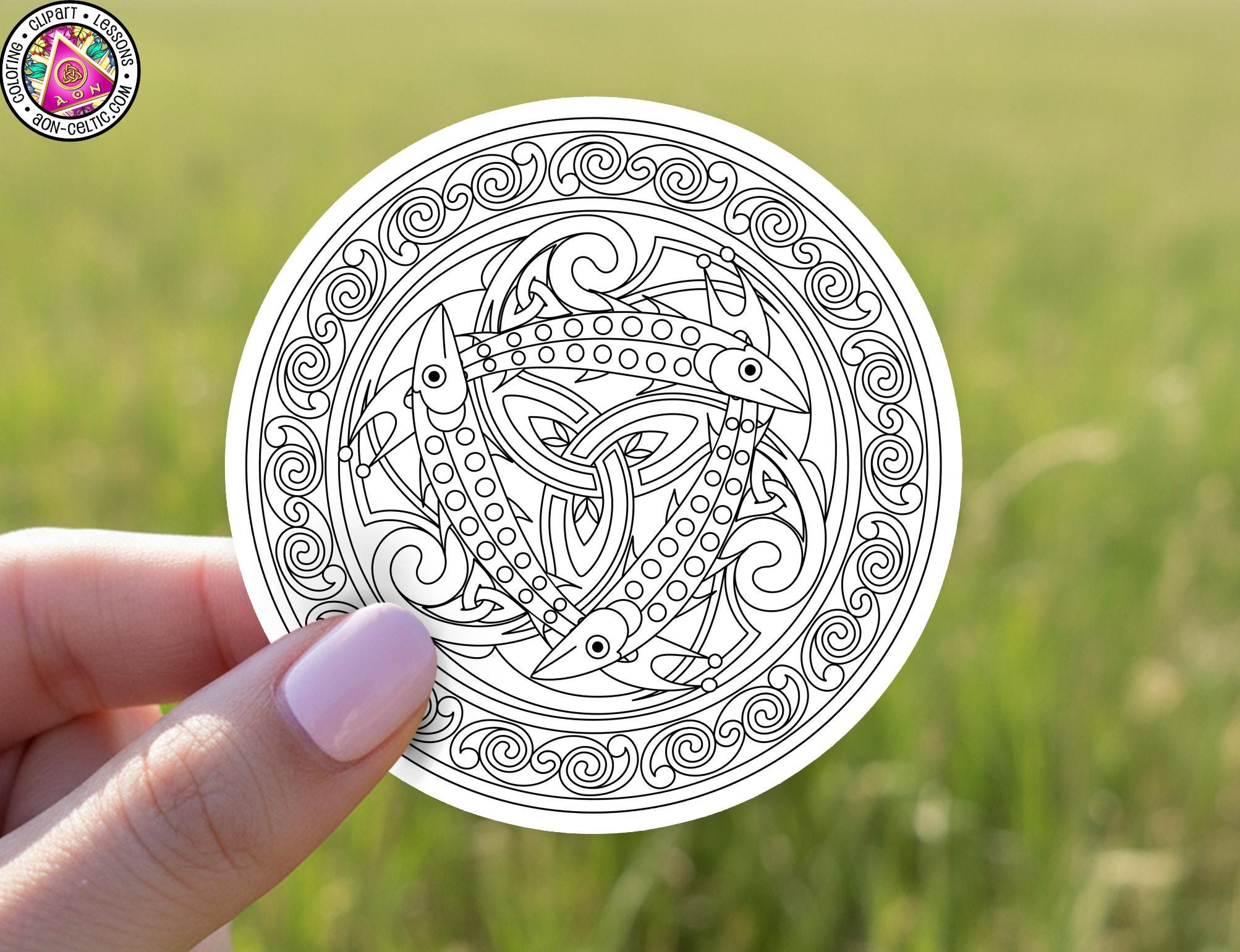 A hand holding a circular sticker with an intricate Celtic knot design.
