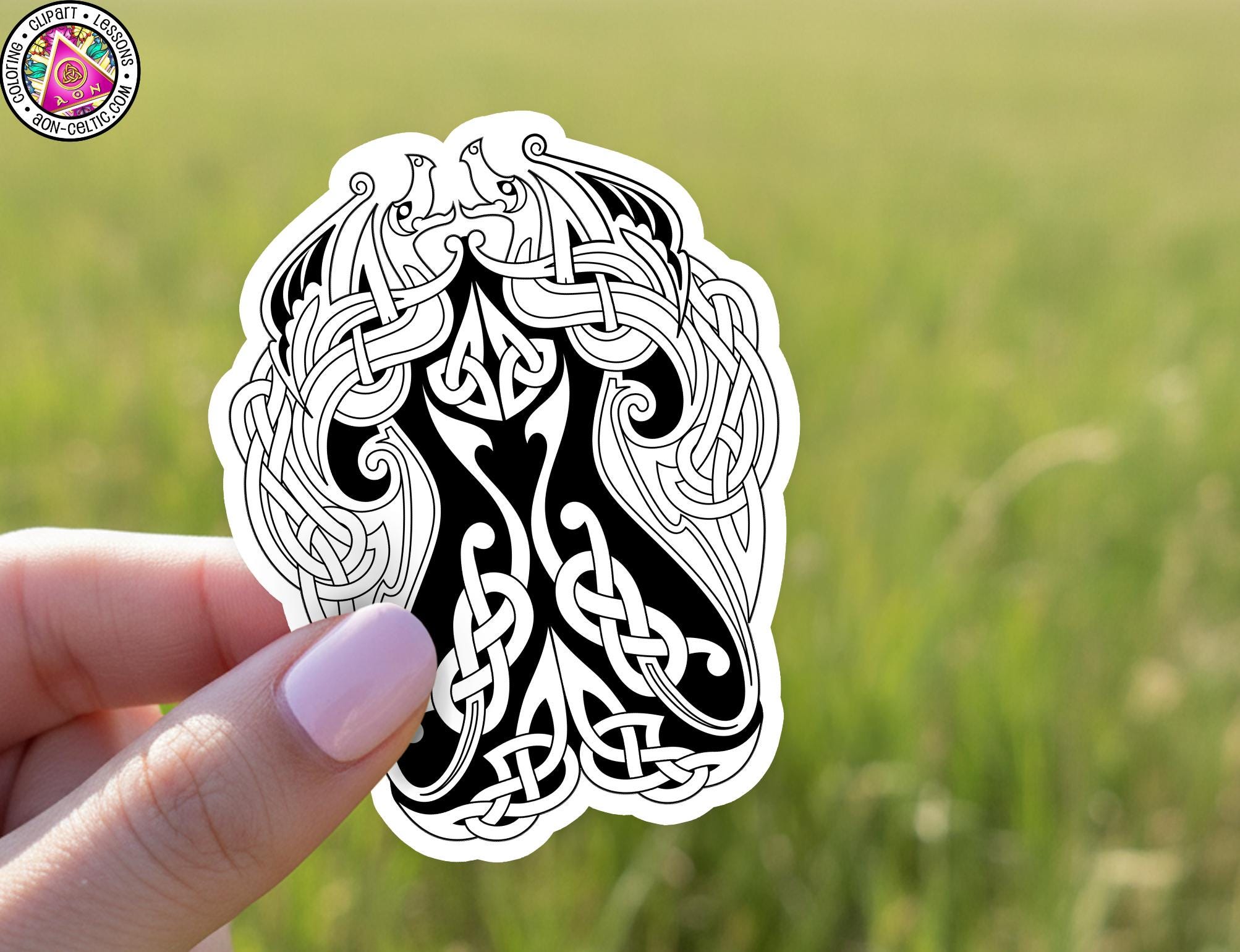 A hand holding a sticker with an intricate, black and white design featuring a stylized, abstract pattern resembling a crescent moon or other celestial shape.