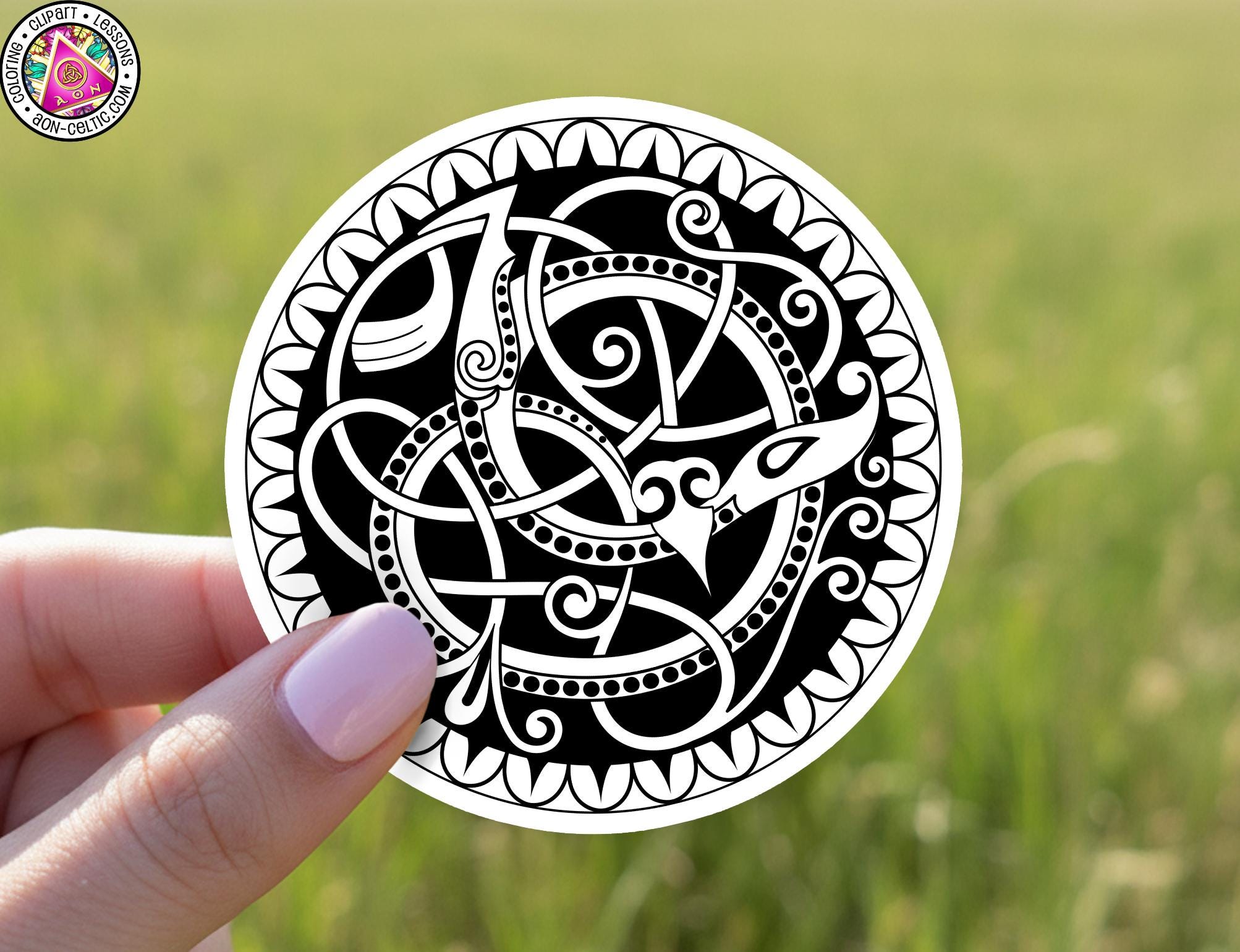 A hand holding a circular sticker with an intricate black and white design featuring a snake and other decorative elements.